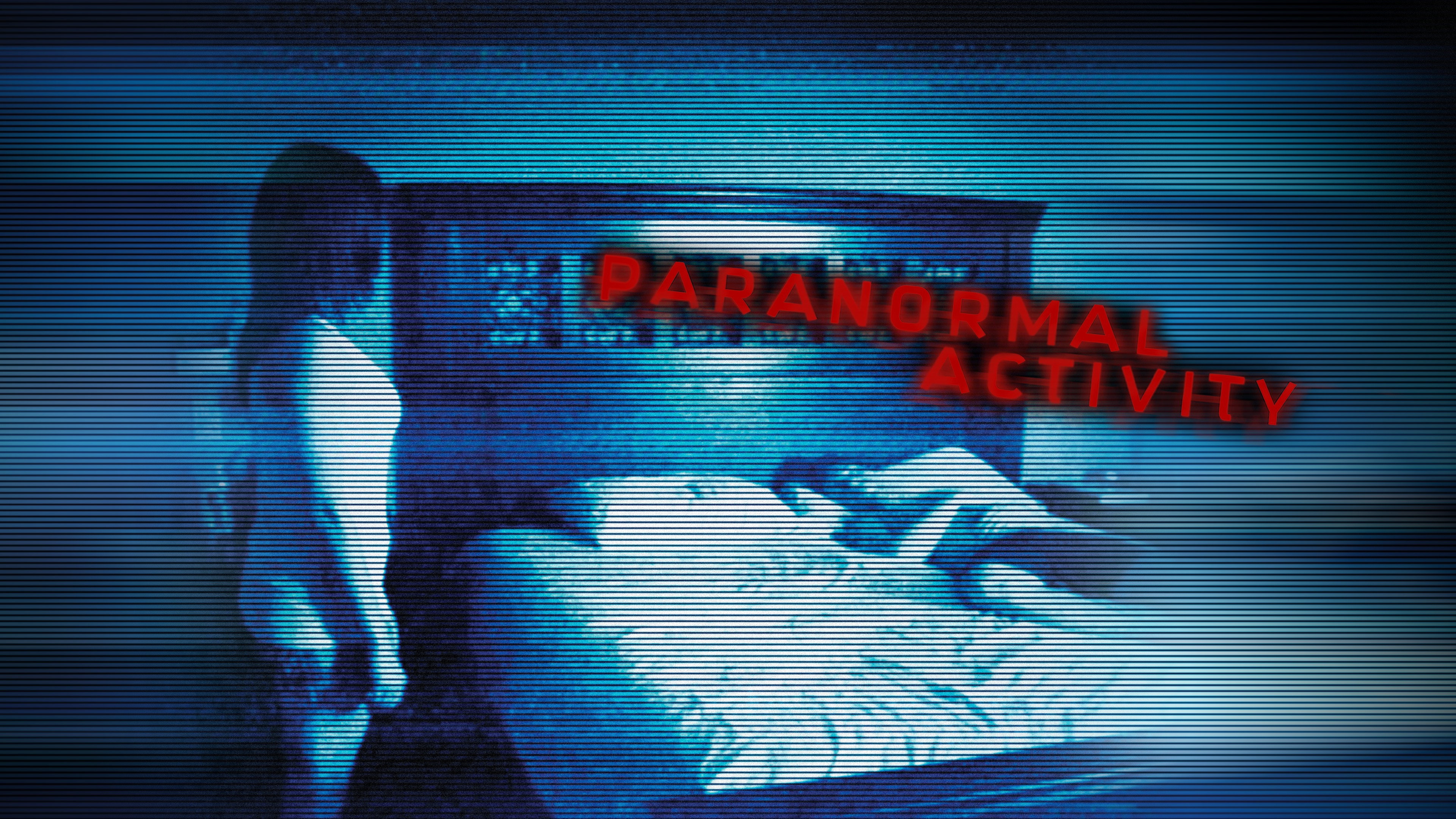 A dimly lit bedroom scene featuring a woman standing beside a bed with a person lying under the covers, with the words 'PARANORMAL ACTIVITY' displayed in red text.