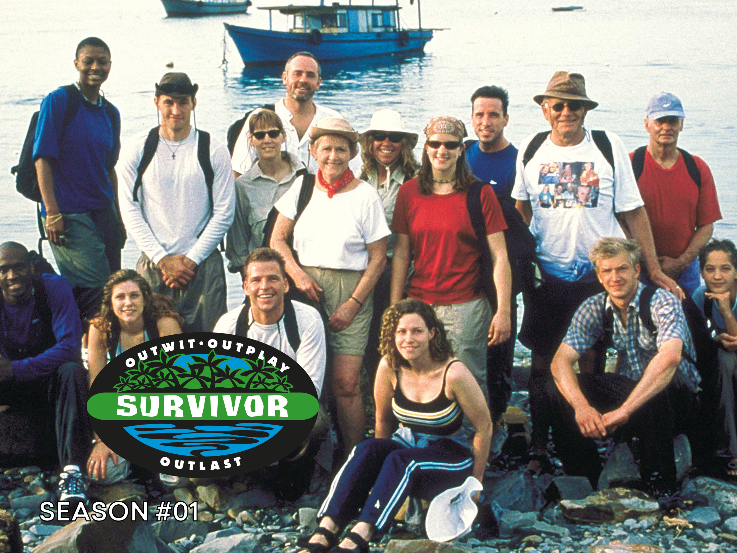 A diverse group of 19 contestants from the first season of Survivor, posing together on a rocky beach with a boat in the background. The Survivor logo and season number are displayed at the bottom.