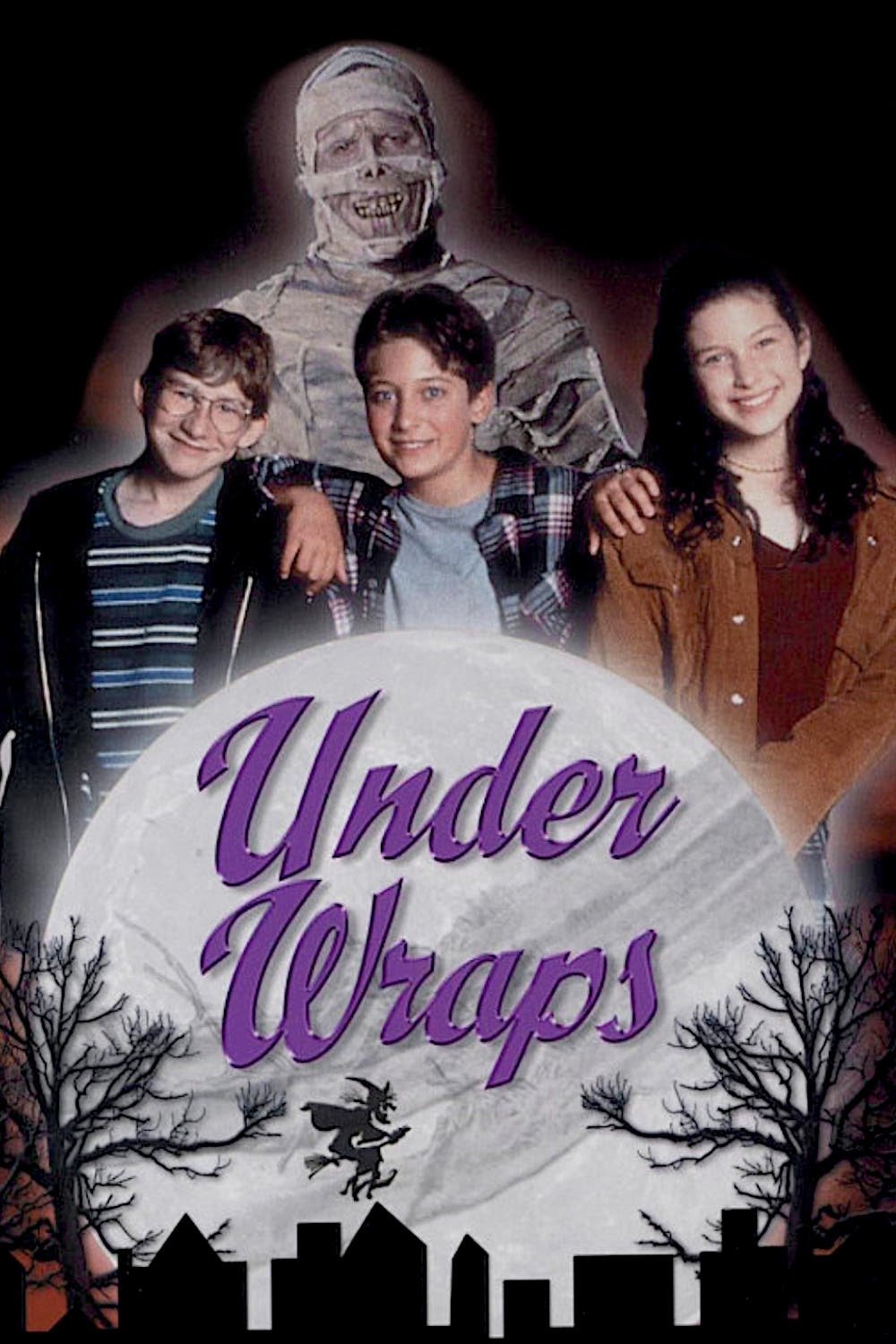 Three children posing together with a friendly mummy in the background. The title 'Under Wraps' is prominently displayed, along with Halloween-themed elements like a moon and silhouettes of trees and buildings.