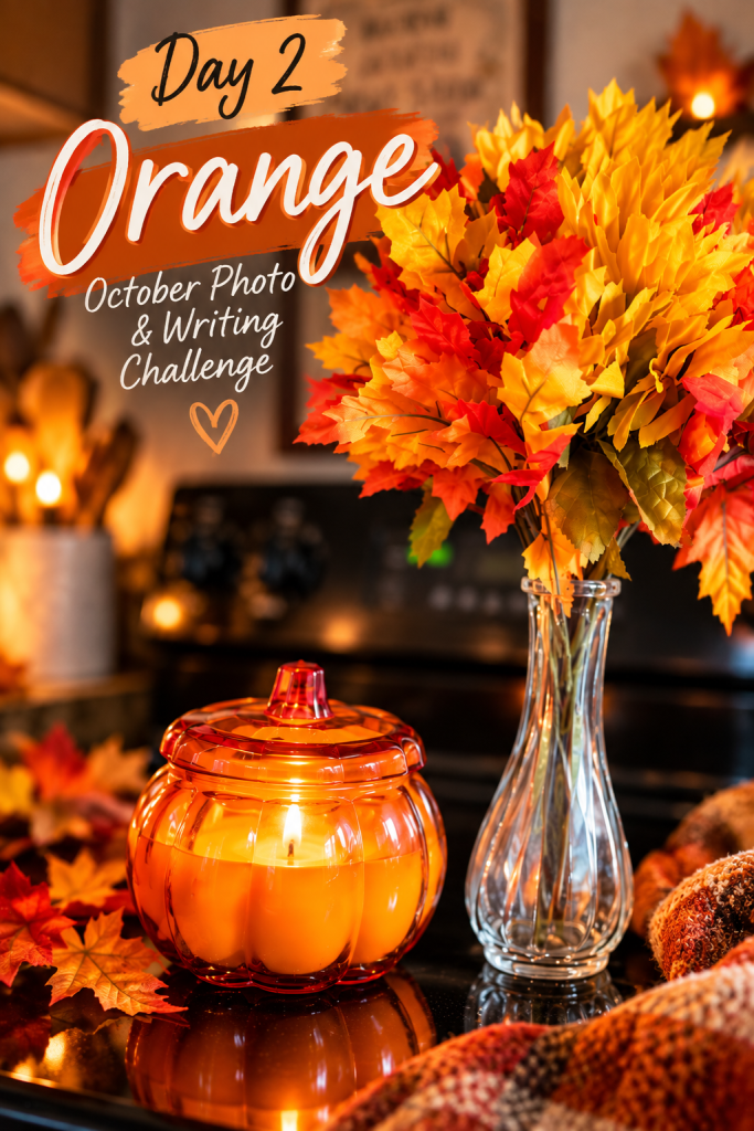 A cozy autumn scene featuring a pumpkin-shaped candle holder with lit candles, surrounded by colorful fall leaves and a glass vase filled with vibrant orange and yellow foliage. The words 'Day 2 Orange' and 'October Photo & Writing Challenge' are displayed prominently.
