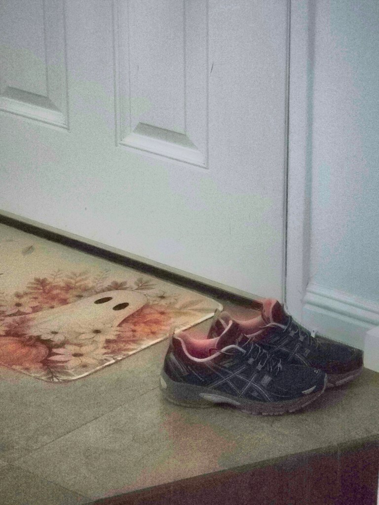 A pair of athletic shoes placed near a white door, with a decorative mat featuring a ghost design visible on the floor.